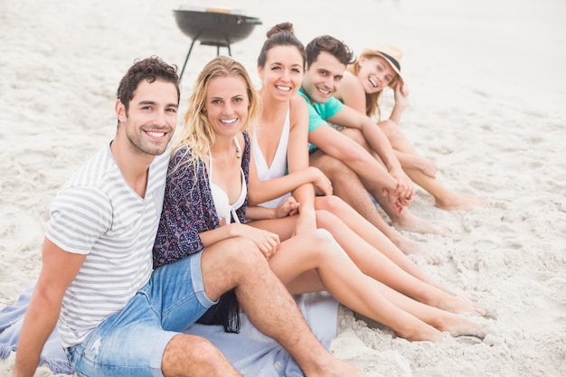 Gruppo di amici seduti fianco a fianco sulla spiaggia