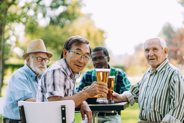 Gruppo di amici senior che bevono una birra al parco. Concetti di stile di vita su anzianità e terza età