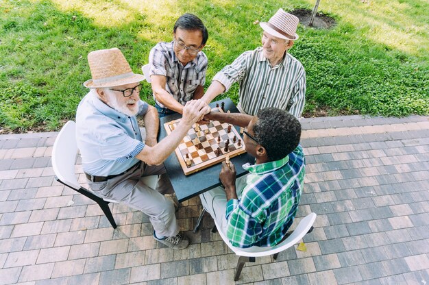 Gruppo di amici senior che giocano a scacchi al parco. Concetti di stile di vita su anzianità e terza età