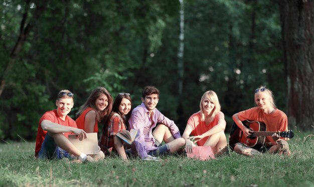 Gruppo di amici studenti con libri e chitarra seduti sull'erba nel parco