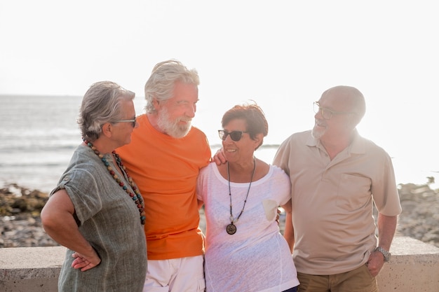 Gruppo di anziani e persone mature in spiaggia che si prendono insieme e si divertono con il mare o l'oceano sullo sfondo - quattro persone