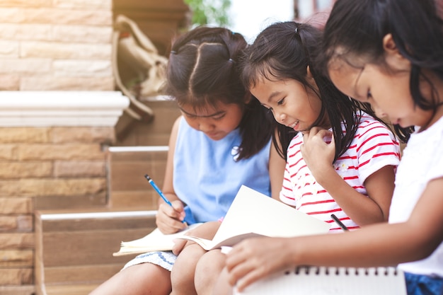 Gruppo di bambini asiatici leggendo un libro e scrivendo insieme un quaderno