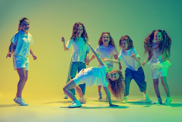 Gruppo di bambini attivi ragazze allegre che ballano isolate su sfondo verde in luce al neon