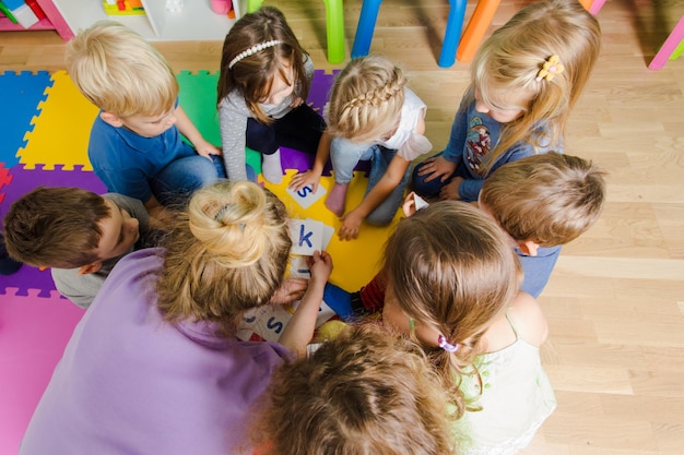 Gruppo di bambini della scuola materna seduti a stretto contatto su un pavimento insieme all'insegnante che fornisce lavoro di gruppo Bambini che imparano a collaborare mentre risolvono compiti