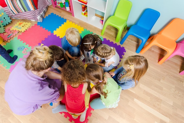 Gruppo di bambini della scuola materna seduti a stretto contatto su un pavimento insieme all'insegnante che fornisce lavoro di gruppo Bambini che imparano a collaborare mentre risolvono compiti