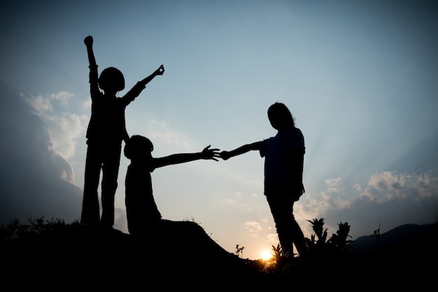 Gruppo di bambini felici che giocano sulla collina al tramonto, silhouette