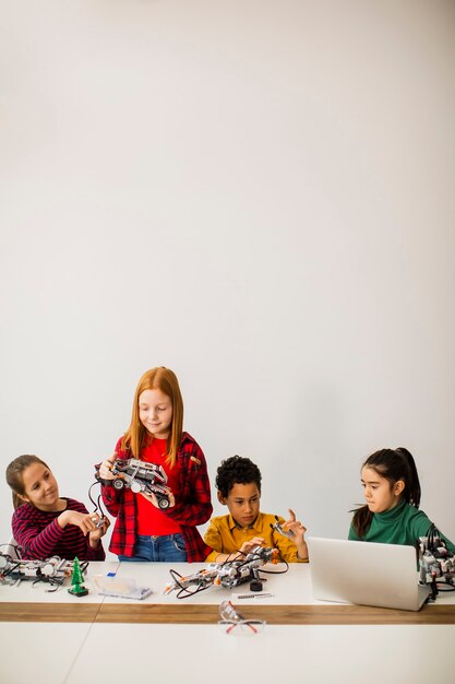 Gruppo di bambini felici che programmano giocattoli elettrici e robot in aula di robotica