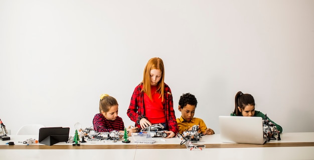 Gruppo di bambini felici che programmano giocattoli elettrici e robot in aula di robotica