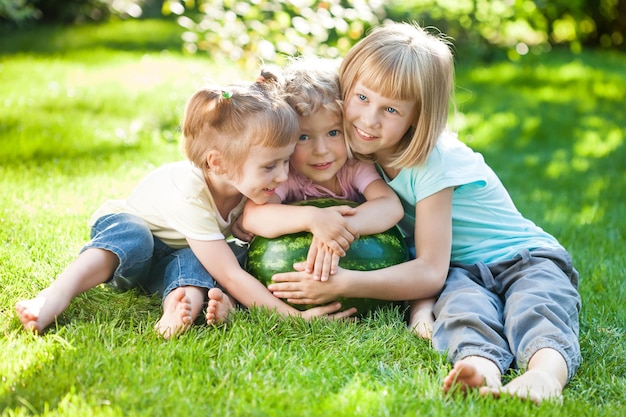 Gruppo di bambini felici con l'anguria che gioca sull'erba verde nel parco estivo