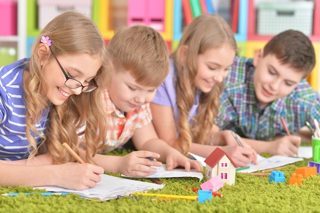 Gruppo di bambini sdraiati sul pavimento con tappeto verde e disegno con le matite