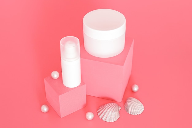 Gruppo di barattoli di crema cosmetica bianca senza marchio in piedi su podi rosa con palline e conchiglie silber. Presentazione del prodotto per la cura della pelle sullo sfondo rosa. Modello alla moda. Cura della pelle, bellezza e spa.