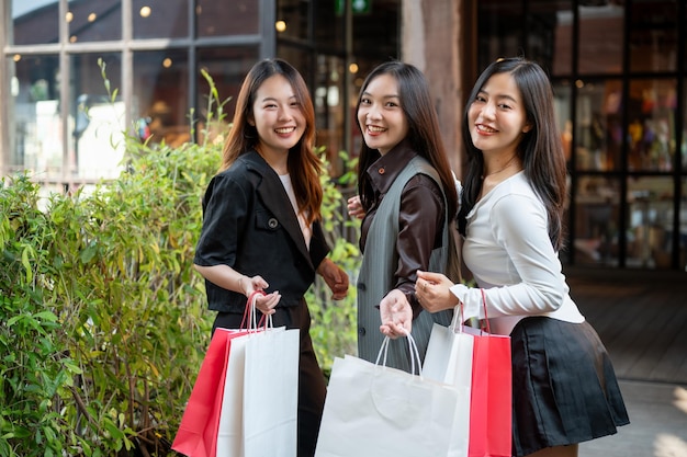 Gruppo di belle amiche asiatiche con le loro borse della spesa che si divertono a fare shopping in città