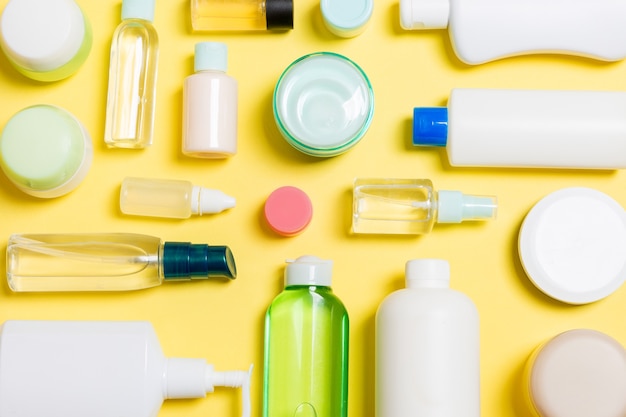 Gruppo di bottiglie di plastica per la cura del corpo Composizione piatta con prodotti cosmetici su sfondo giallo spazio vuoto per la progettazione. Set di contenitori cosmetici bianchi, vista dall'alto con spazio di copia.