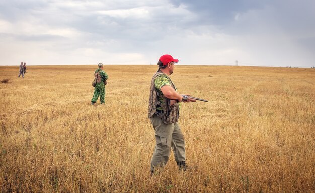 Gruppo di cacciatori con pistole che si muovono attraverso il campo, in cerca di prede