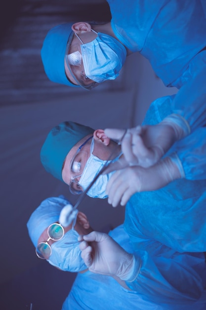 Gruppo di chirurghi al lavoro in sala operatoria dai toni blu Equipe medica che esegue l'operazione