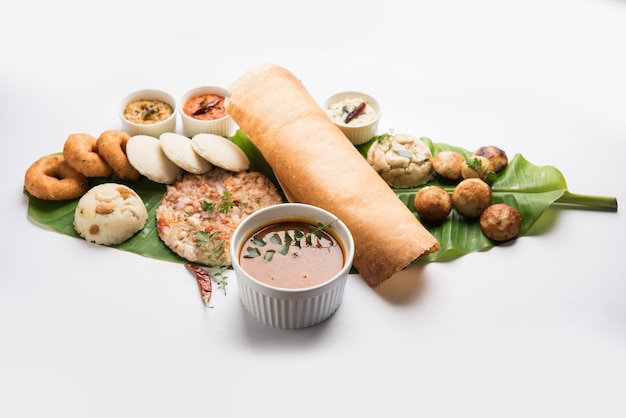 Gruppo di cibo dell'India meridionale come Masala Dosa, Uttapam, Idli o pigramente, Wada o vada, sambar, appam, semolina halwa, upma servito su foglie di banana con chutney colorati, messa a fuoco selettiva