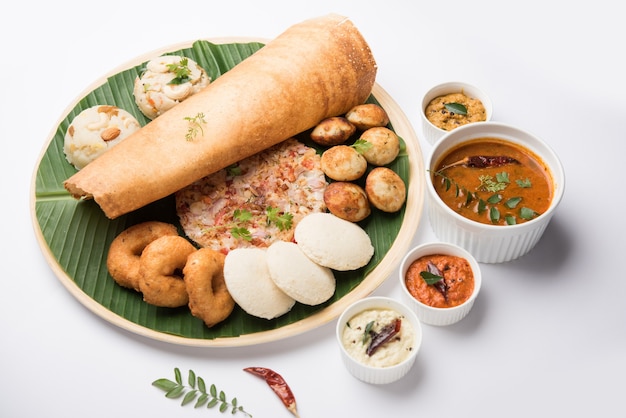 Gruppo di cibo dell'India meridionale come Masala Dosa, Uttapam, Idli o pigramente, Wada o vada, sambar, appam, semolina halwa, upma servito su foglie di banana con chutney colorati, messa a fuoco selettiva