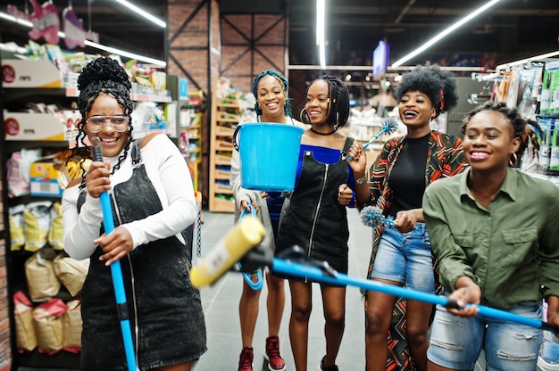 Gruppo di cinque donne con scopa per la polvere, scopino e secchio che si divertono nel dipartimento degli articoli per la pulizia della casa in un supermercato