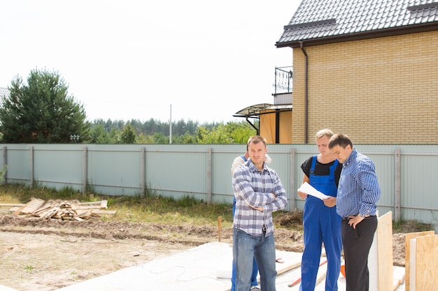 Gruppo di costruttori e ingegneri del sito in piedi a discutere i dettagli su un terreno residenziale sgomberato sulle fondamenta di una nuova casa