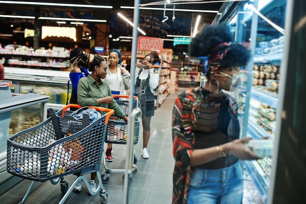 Gruppo di donne africane con carrelli vicino a scaffale frigorifero che vende cartone di uova di prodotti lattiero-caseari nel supermercato