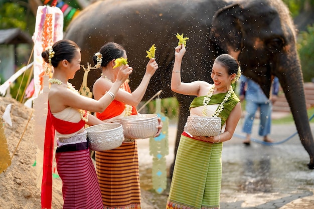 Gruppo di donne thailandesi in abito tradizionale thailandese che giocano a spruzzare acqua con un elefante all'aperto