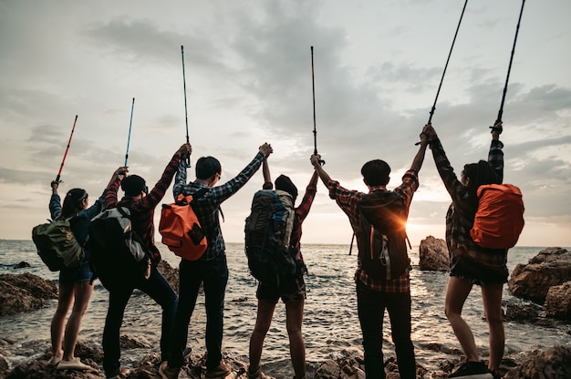 Gruppo di escursionisti che alzano le braccia in riva al mare al tramonto visto da dietroTeamwork e avventura