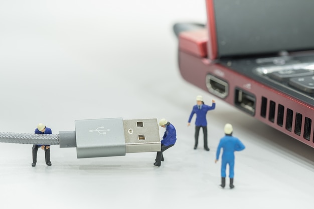 Gruppo di figure in miniatura di lavoratore che lavorano su cavo USB con computer portatile