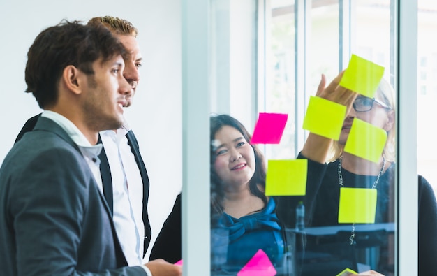 Gruppo di gente del collega di affari che si incontra discutendo idea di lavoro in note appiccicose sulla parete di vetro all&#39;ufficio