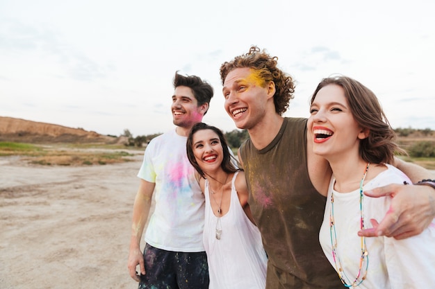 Gruppo di giovani amici allegri che si divertono in spiaggia con colorati holi paint