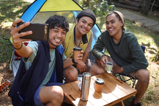 Gruppo di giovani amici asiatici che prendono selfie con lo smartphone registrando il vlog di viaggio durante il campeggio al mo