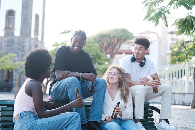 Gruppo di giovani amici che bevono qualche birra all'aperto seduti su una panchina in un brindisi di amicizia stile di vita cittadino º