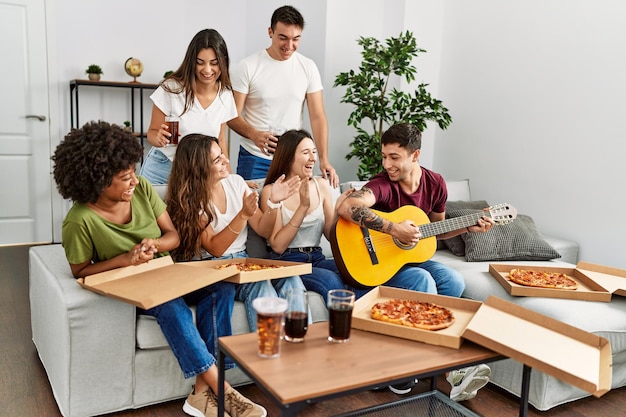 Gruppo di giovani amici che fanno festa mangiando pizza italiana e suonando la chitarra classica a casa.