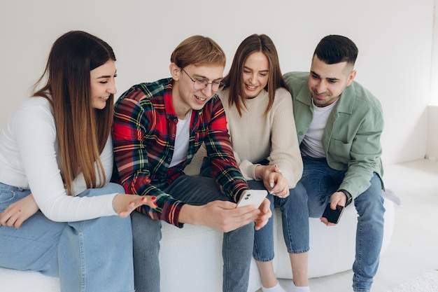 Gruppo di giovani amici felici che guardano video sul telefono mentre si siedono sul divano all'interno