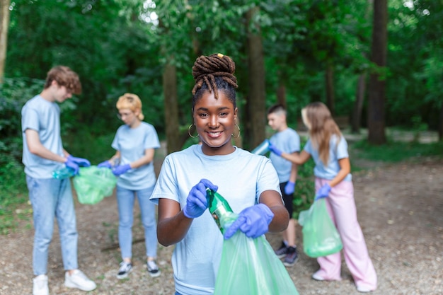 Gruppo di giovani amici volontari che raccolgono bottiglie di plastica per i sacchetti della spazzatura nella foresta Concetto di ecologia