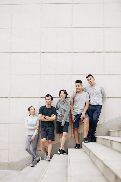 Gruppo di giovani asiatici felici in piedi sui gradini dopo aver fatto jogging all'aperto insieme