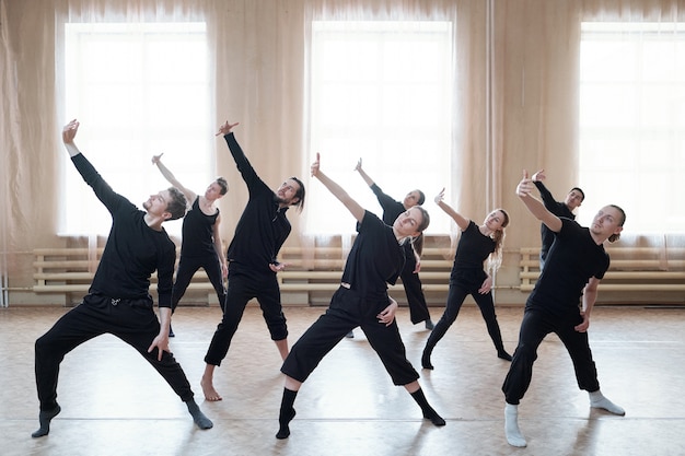Gruppo di giovani ballerini attivi in magliette nere e pantaloni che allungano un braccio davanti a se stessi durante l'esercizio di danza