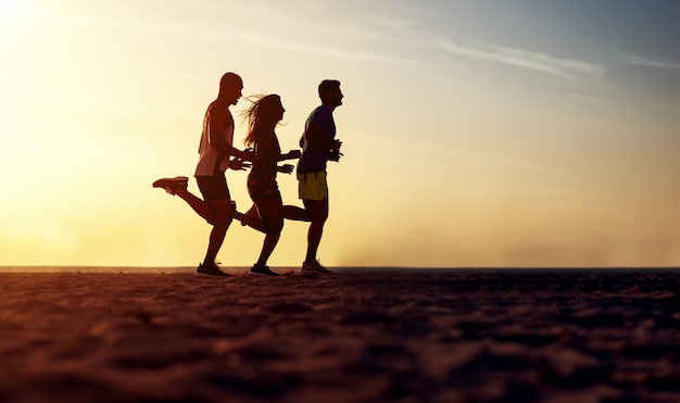 Gruppo di giovani che corrono alla spiaggia sul tramonto di bella estate.
