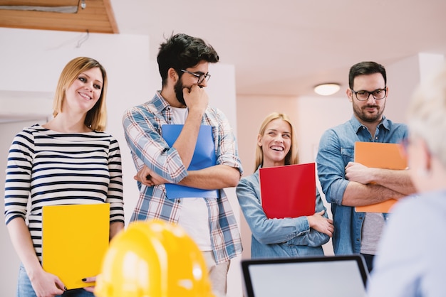 Gruppo di giovani che si divertono in attesa in fila con le cartelle per un colloquio di lavoro.