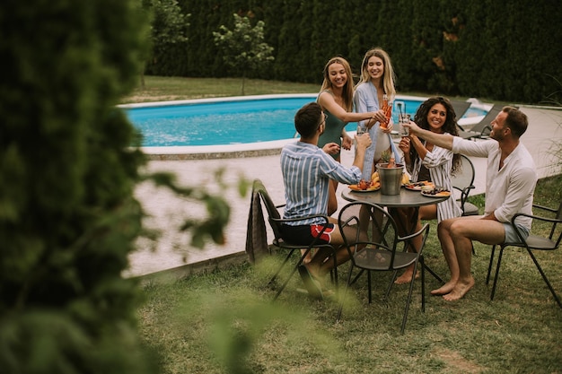 Gruppo di giovani che tifo con sidro a bordo piscina in giardino