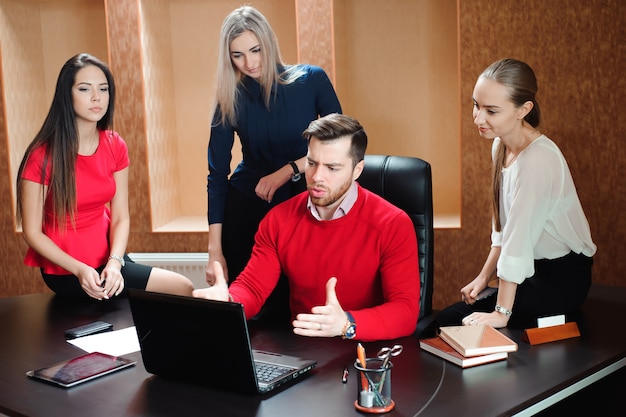 Gruppo di giovani colleghi che per mezzo del computer portatile all'ufficio.