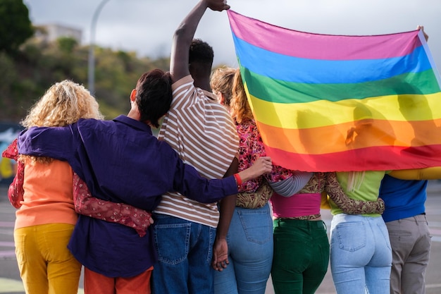 Gruppo di giovani da dietro che tengono la bandiera arcobaleno LGBTI