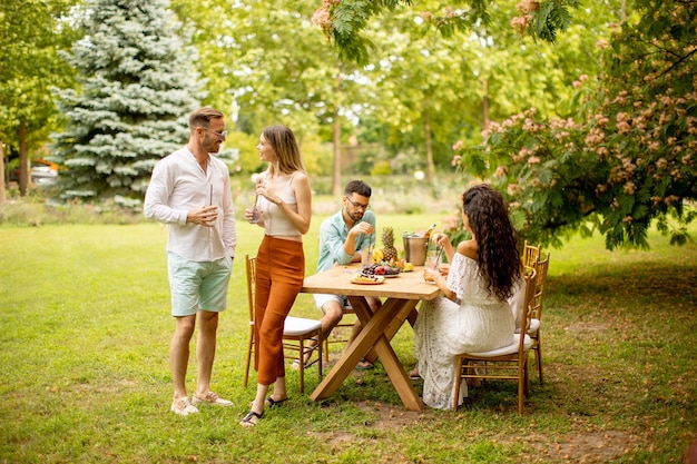 Gruppo di giovani felici che fanno il tifo con limonata fresca e mangiano frutta in giardino