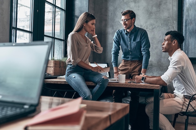 Gruppo di giovani in abbigliamento casual intelligente che discutono di affari mentre lavorano in ufficio