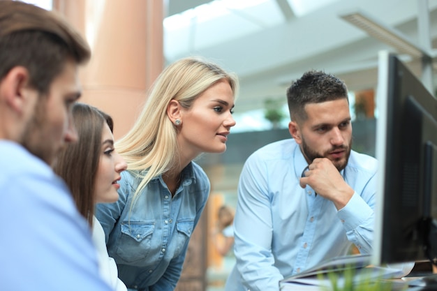 Gruppo di giovani in abbigliamento casual seduti alla scrivania dell'ufficio e discutendo di qualcosa mentre guardano insieme il PC.