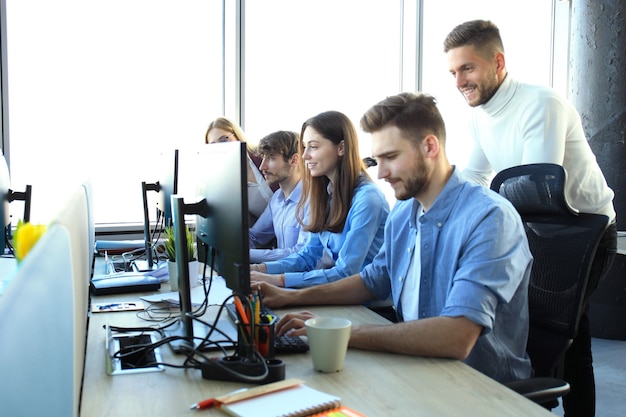 Gruppo di giovani in abbigliamento casual seduti alla scrivania dell'ufficio e discutono di qualcosa mentre guardano insieme il PC.