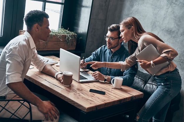 Gruppo di giovani moderni in abbigliamento casual intelligente che utilizzano laptop mentre lavorano in ufficio