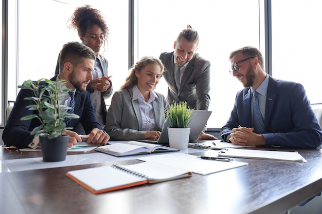 Gruppo di giovani moderni in abiti da cerimonia che sorridono e discutono di qualcosa mentre lavorano nell'ufficio moderno.