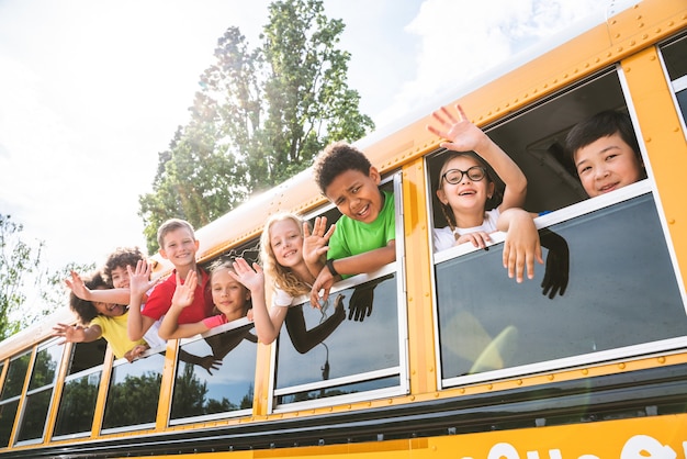 Gruppo di giovani studenti che frequentano la scuola primaria su uno scuolabus giallo - Bambini delle scuole elementari che si divertono