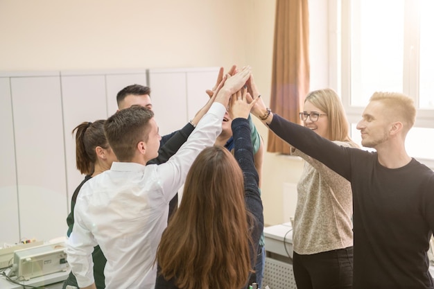 Gruppo di giovani studenti in aula di elettronica che celebrano con successo il progetto finito tenendo le mani insieme, concetto di istruzione e tecnologia