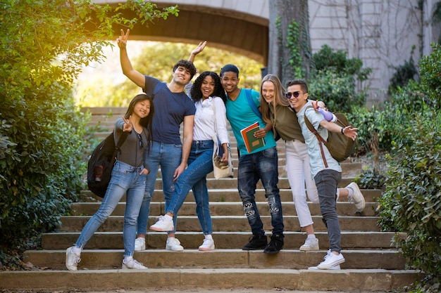 Gruppo di giovani studenti multirazziali universitari che salutano la telecamera su alcune scale